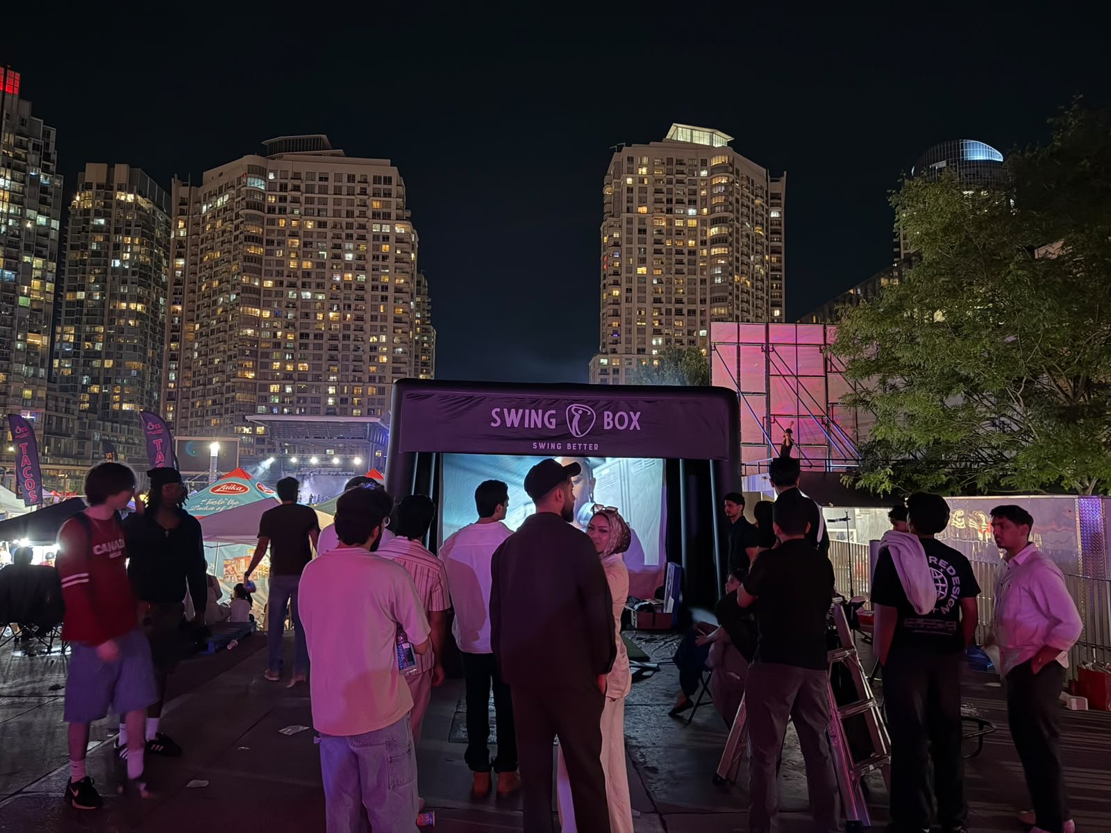 Guests gathered around the Swing Box simulator during a busy outdoor night event