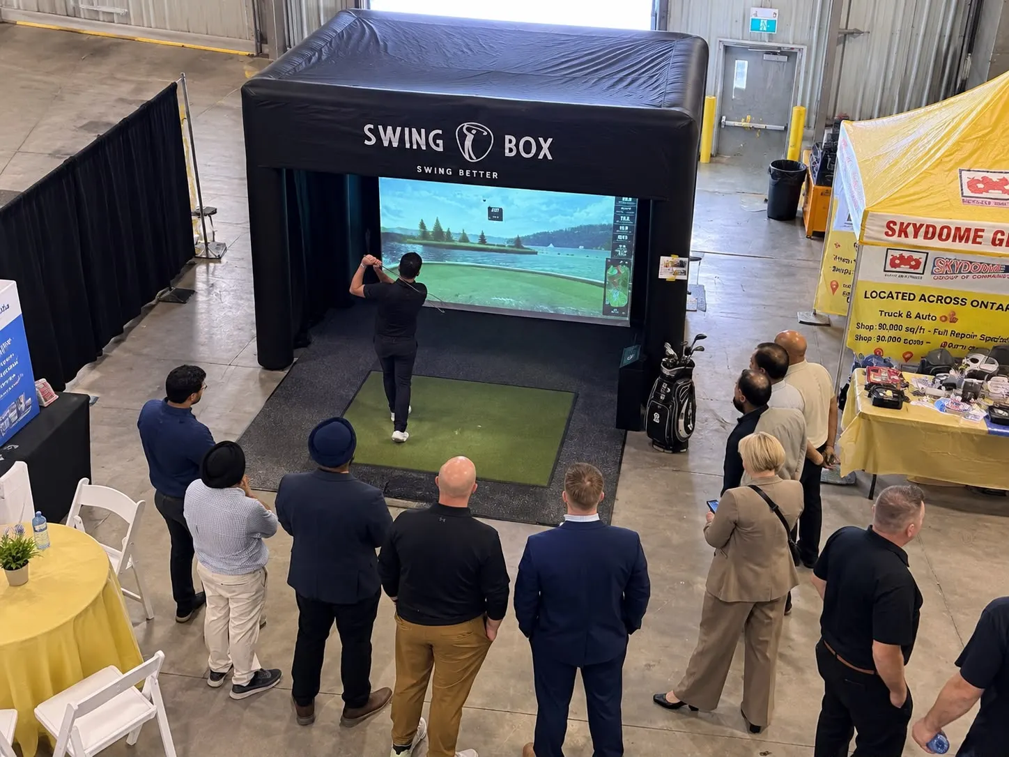 Guests watching a golfer take a shot inside the Swing Box simulator at an indoor event