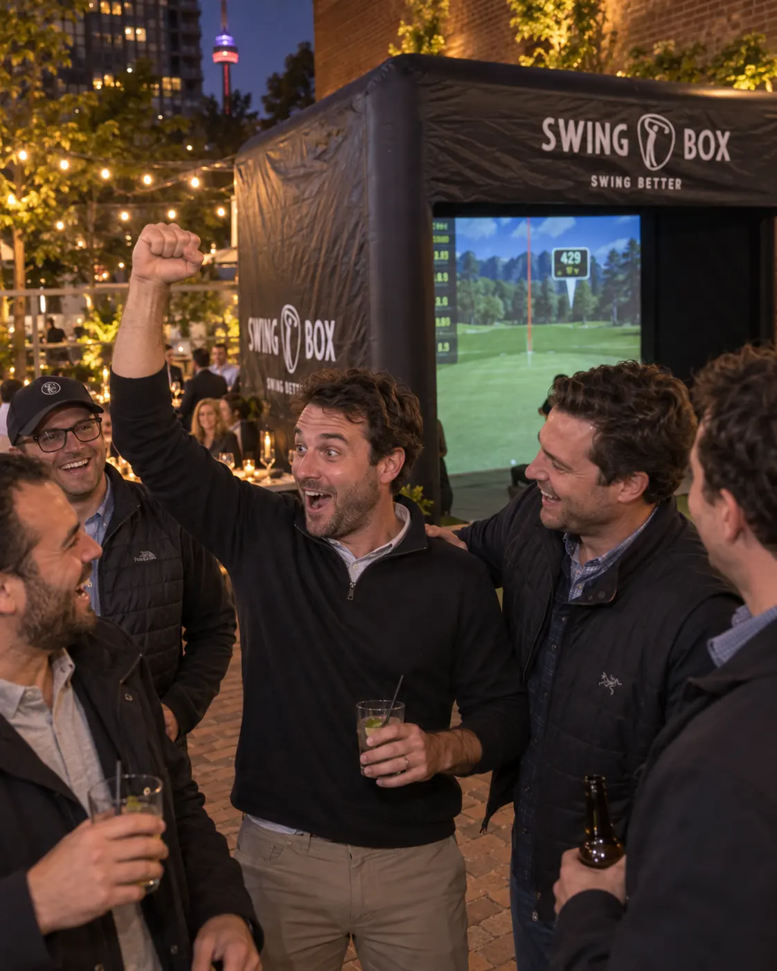 Coworkers react to a winning golf shot beside Swing Box at an evening company gathering